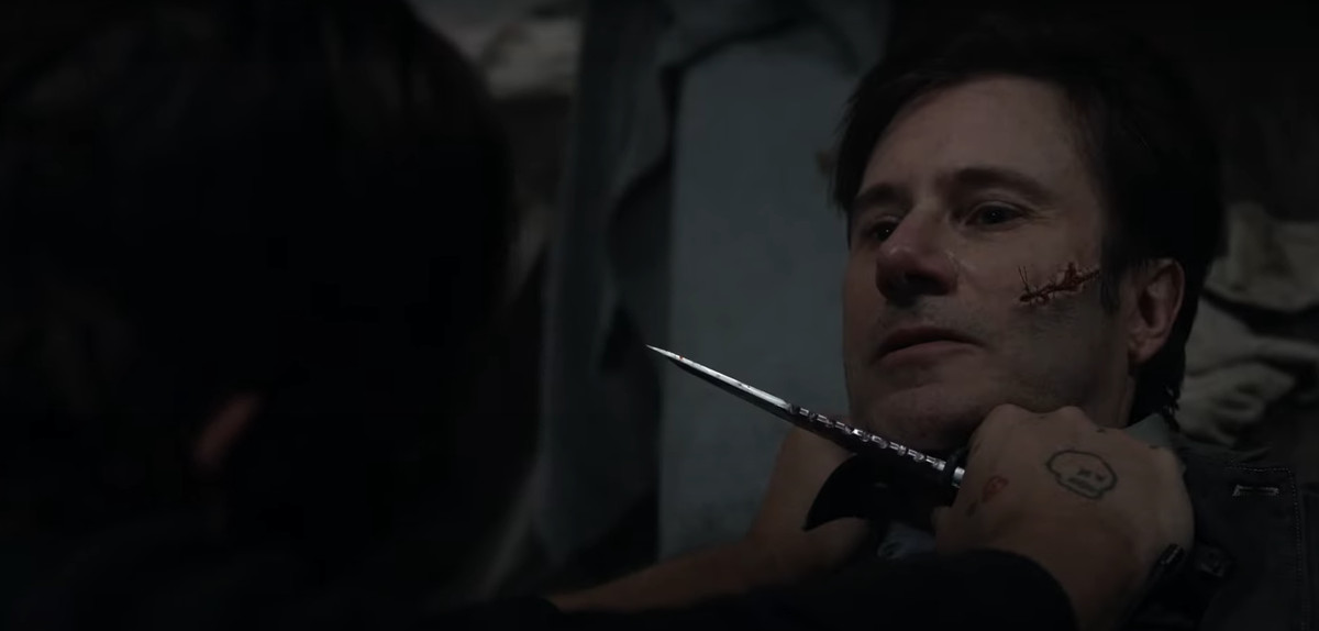 Daryl de The Walking Dead sostiene un cuchillo en la garganta de un hombre con un gran corte en la mejilla que ha sido cosido.